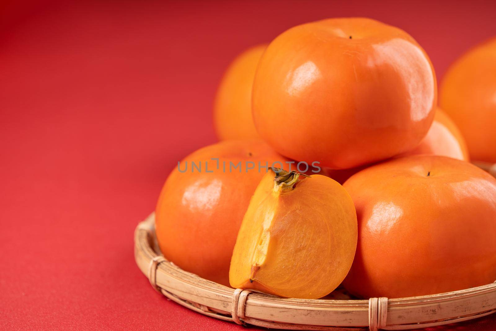 Fresh beautiful sliced sweet persimmon kaki isolated on red table background and bamboo sieve, Chinese lunar new year design concept, close up.