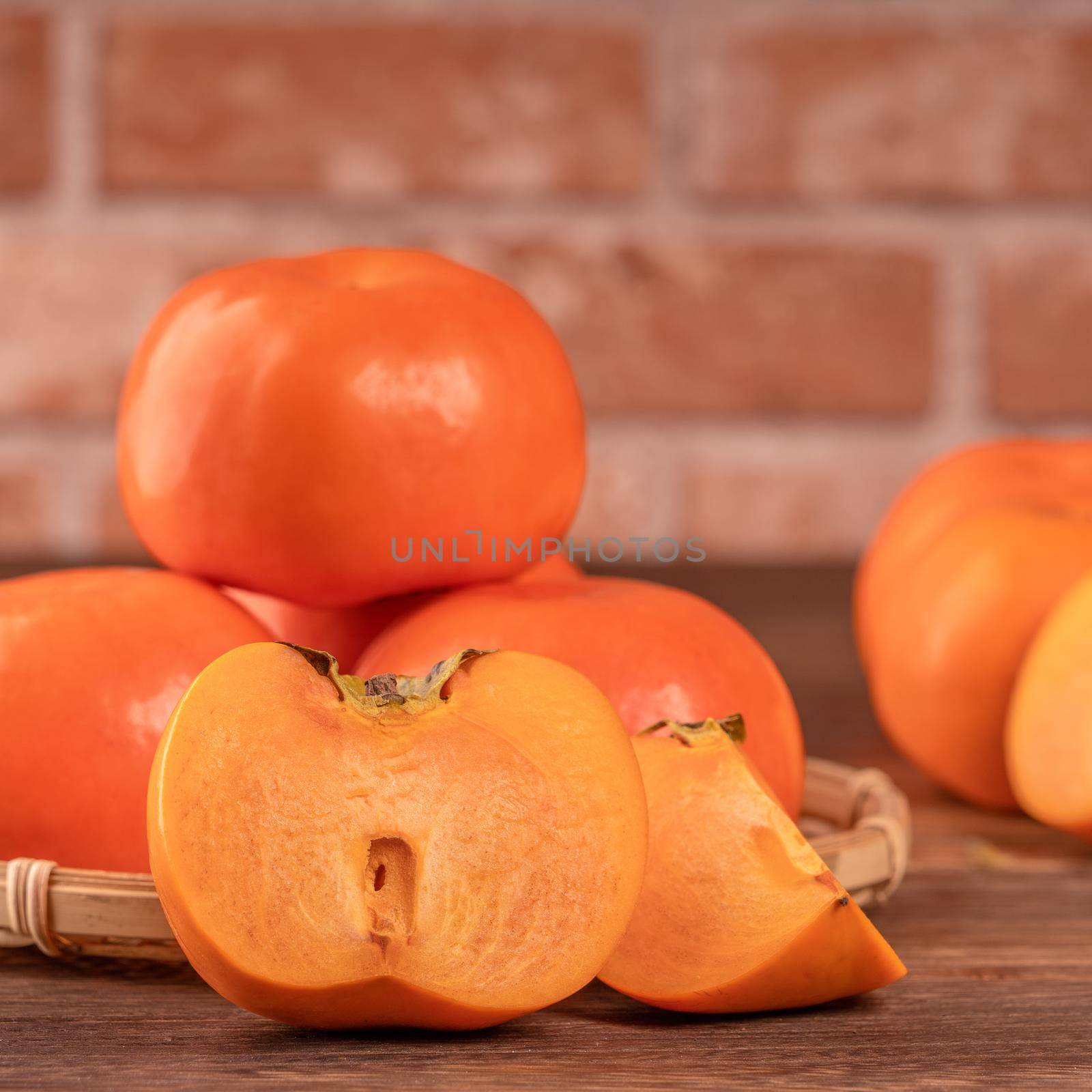Fresh beautiful sliced sweet persimmon kaki on dark wooden table with red brick wall background, Chinese lunar new year fruit design concept, close up.