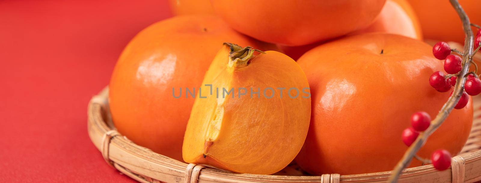 Fresh beautiful sliced sweet persimmon kaki isolated on red table background and bamboo sieve, Chinese lunar new year design concept, close up. by ROMIXIMAGE