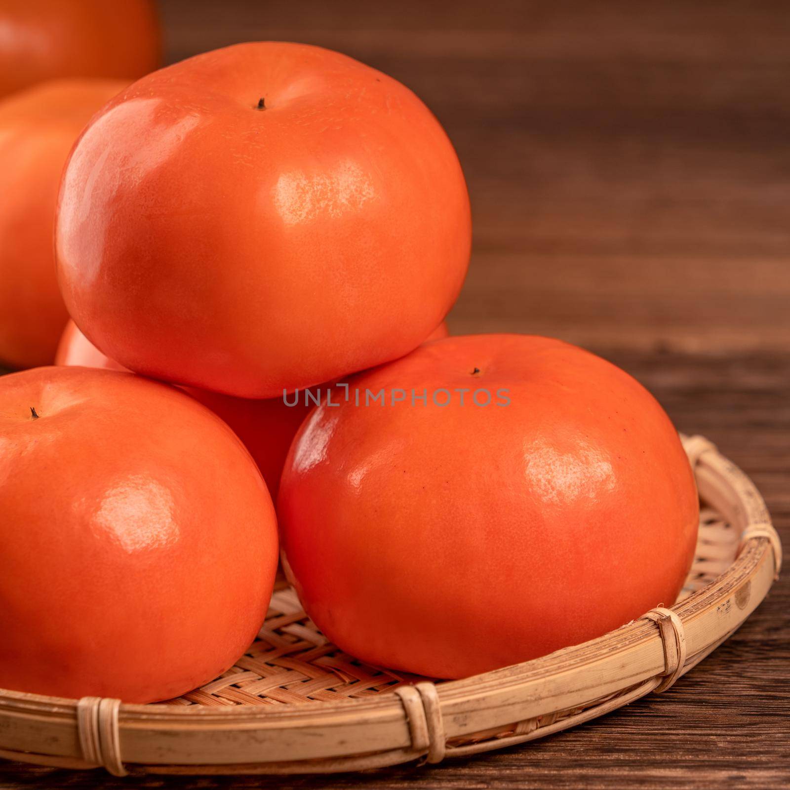 Sliced sweet persimmon kaki in a bamboo sieve basket on dark wooden table with red brick wall background, Chinese lunar new year fruit design concept, close up. by ROMIXIMAGE