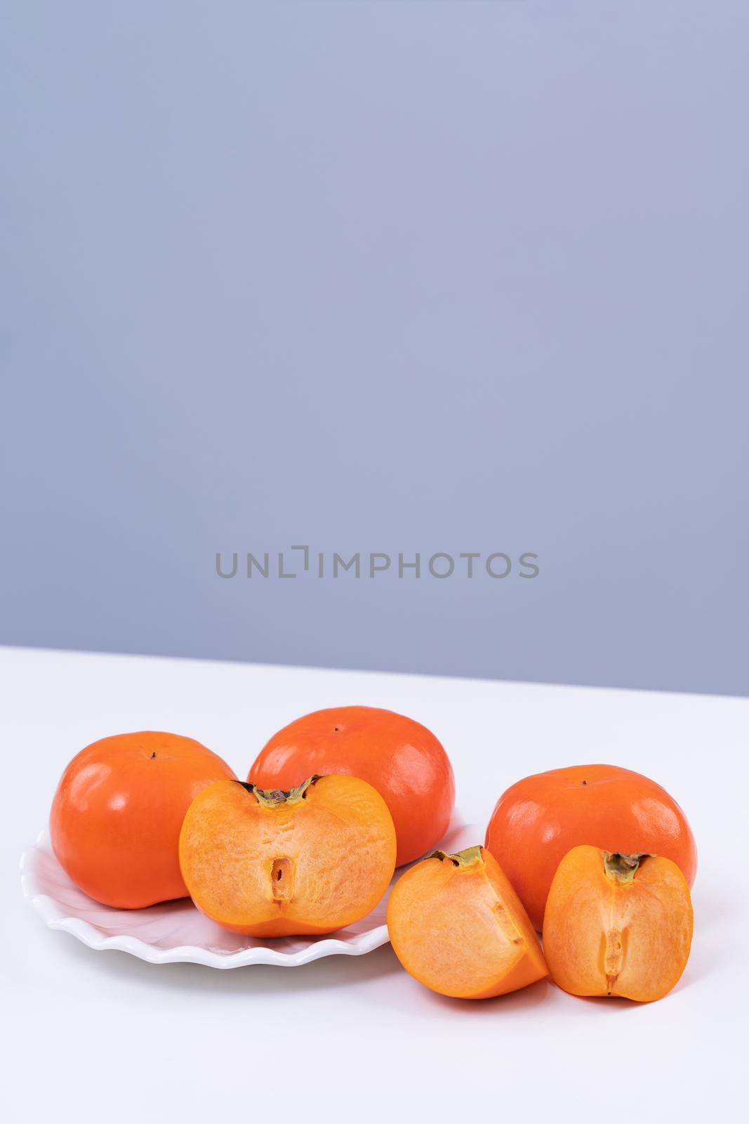 Fresh beautiful sliced sweet persimmon kaki isolated on white kitchen table with gray blue background, Chinese lunar new year design concept, close up.