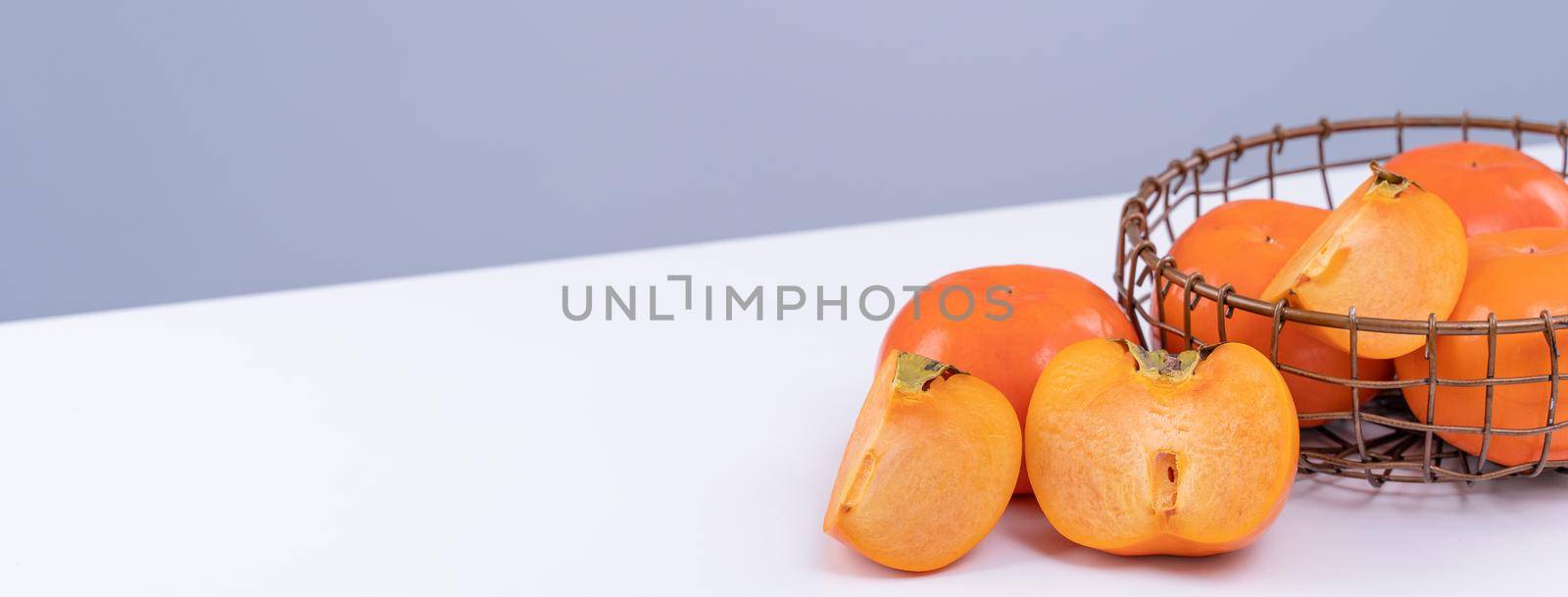 Fresh beautiful sliced sweet persimmon kaki isolated on white kitchen table with gray blue background, Chinese lunar new year design concept, close up.