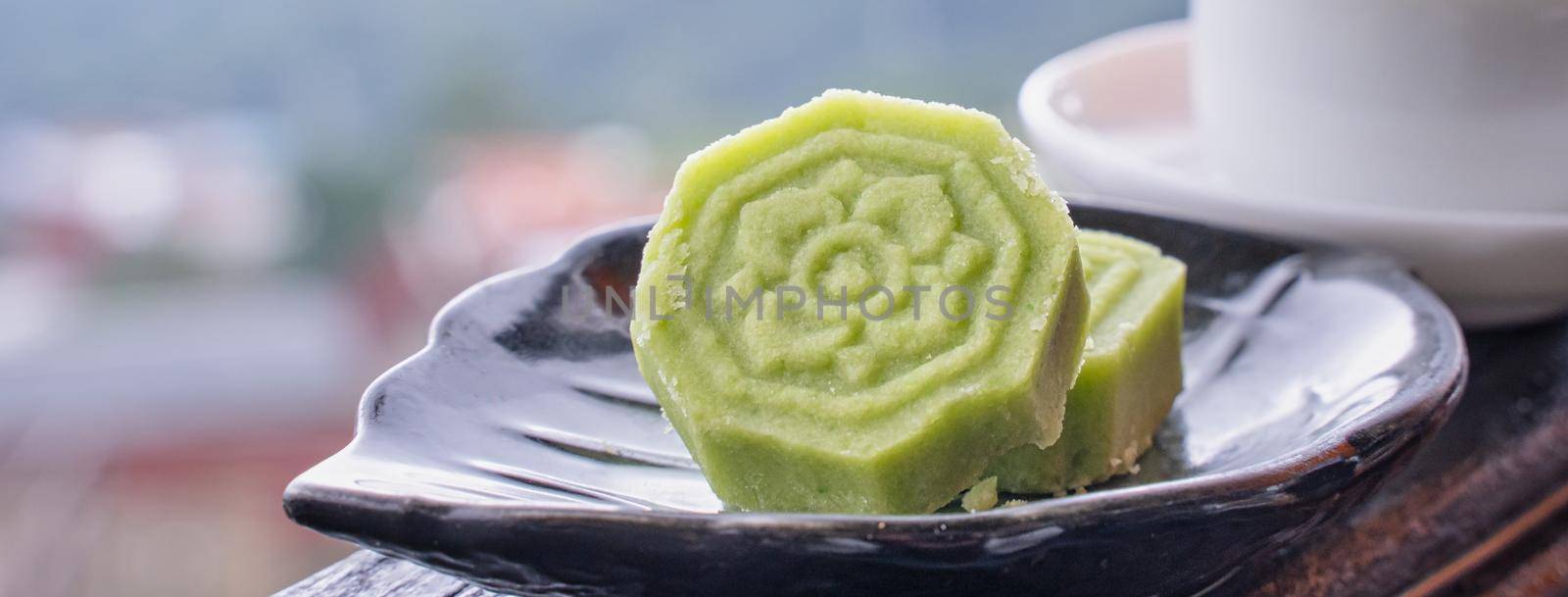 Delicious green mung bean cake with black tea plate on wooden railing of a teahouse in Taiwan with beautiful landscape in background, close up.