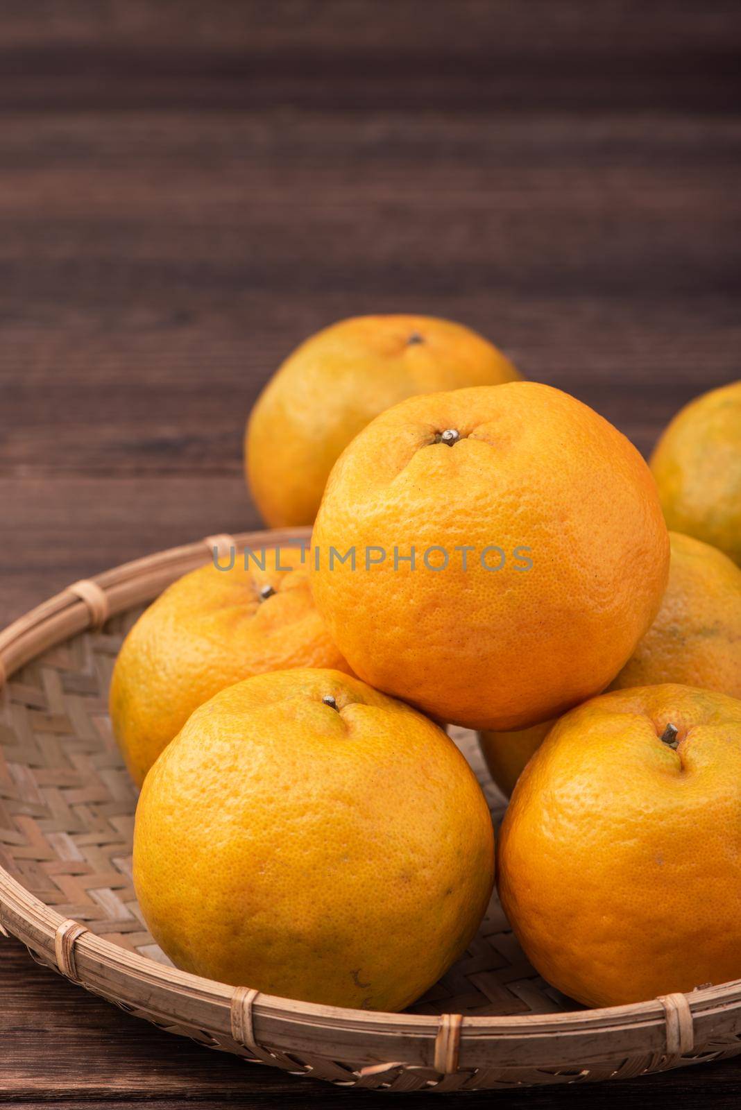 Fresh, beautiful orange color tangerine on bamboo sieve over dark wooden table. Seasonal, traditional fruit of Chinese lunar new year, close up. by ROMIXIMAGE