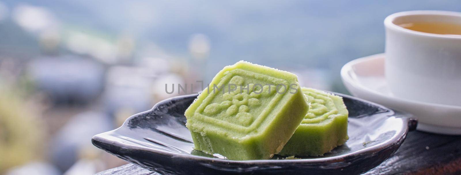 Delicious green mung bean cake with black tea plate on wooden railing of a teahouse in Taiwan with beautiful landscape in background, close up.