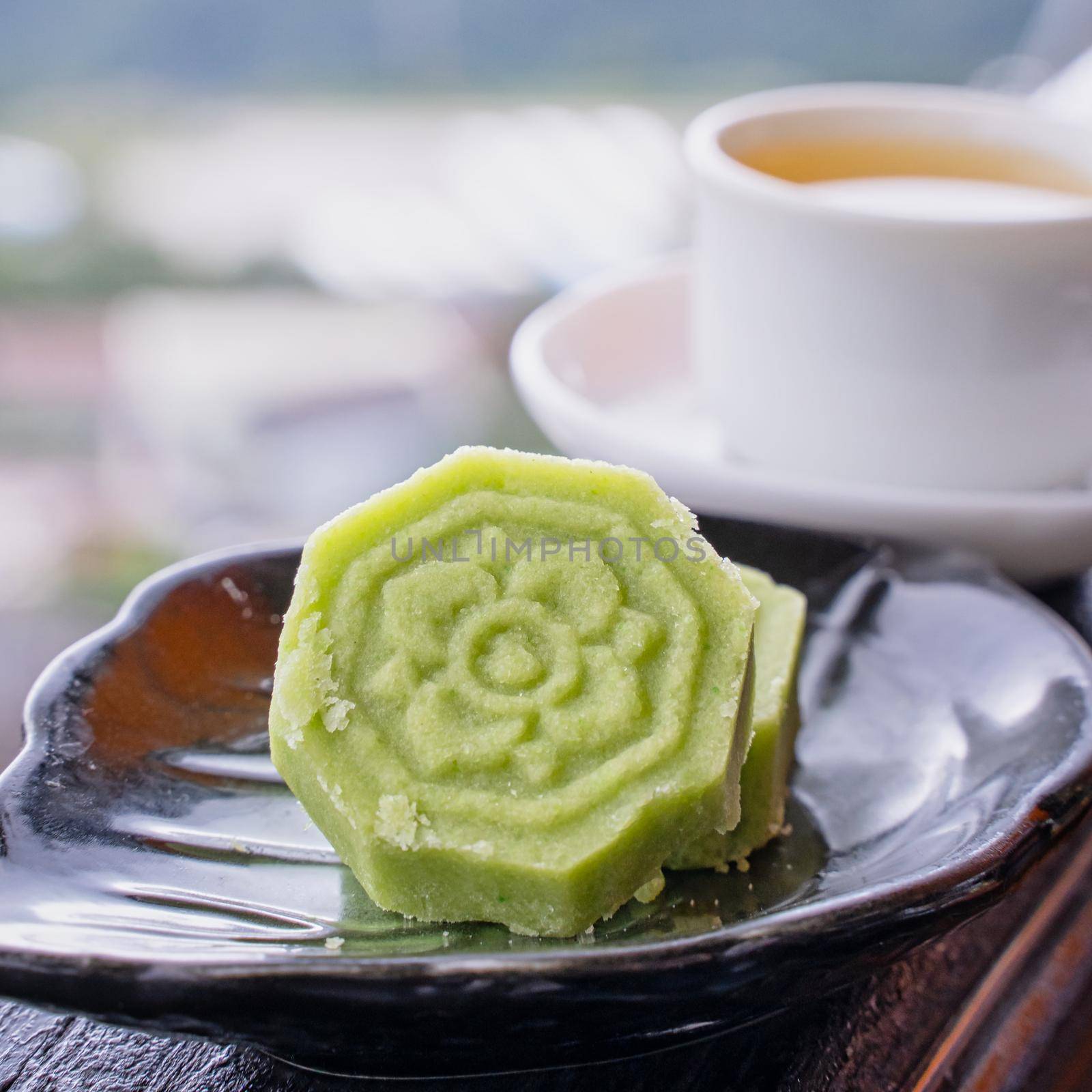 Delicious green mung bean cake with black tea plate on wooden railing of a teahouse in Taiwan with beautiful landscape in background, close up.