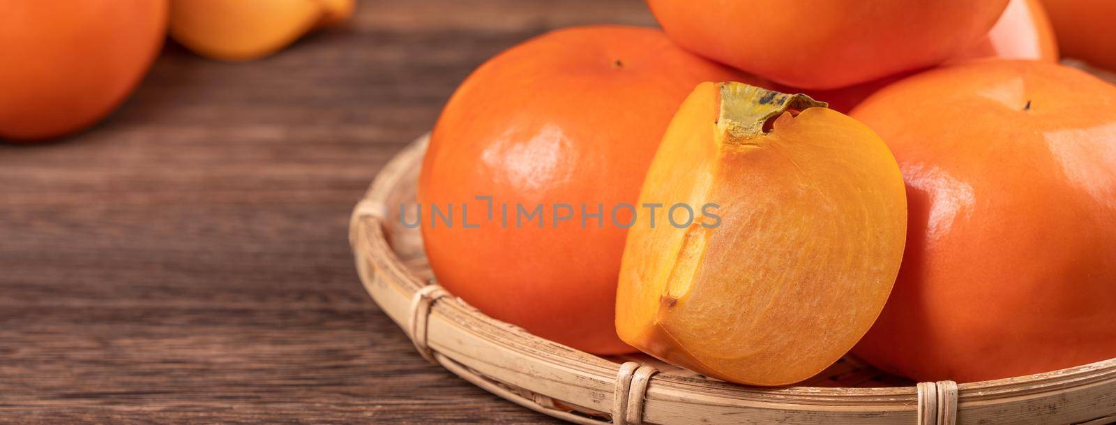 Fresh, beautiful orange color persimmon kaki on bamboo sieve over dark wooden table. Seasonal, traditional fruit of Chinese lunar new year, close up.