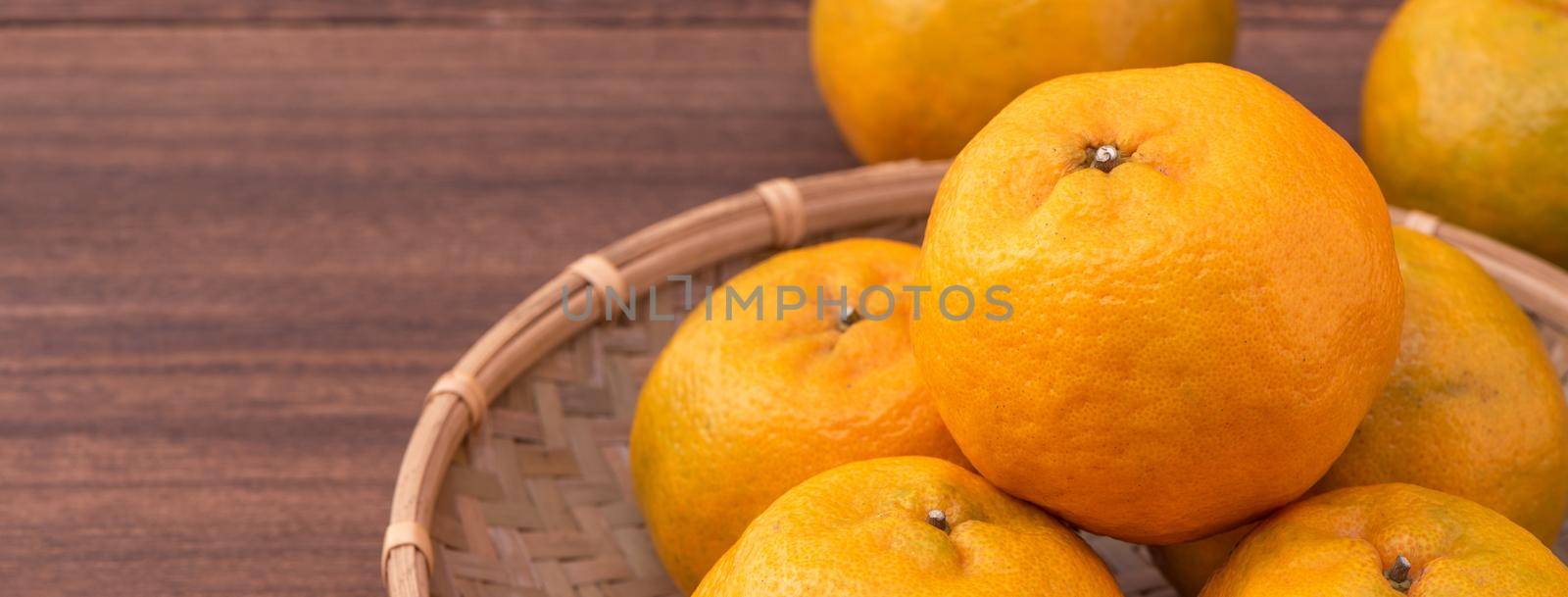 Fresh, beautiful orange color tangerine on bamboo sieve over dark wooden table. Seasonal, traditional fruit of Chinese lunar new year, close up.