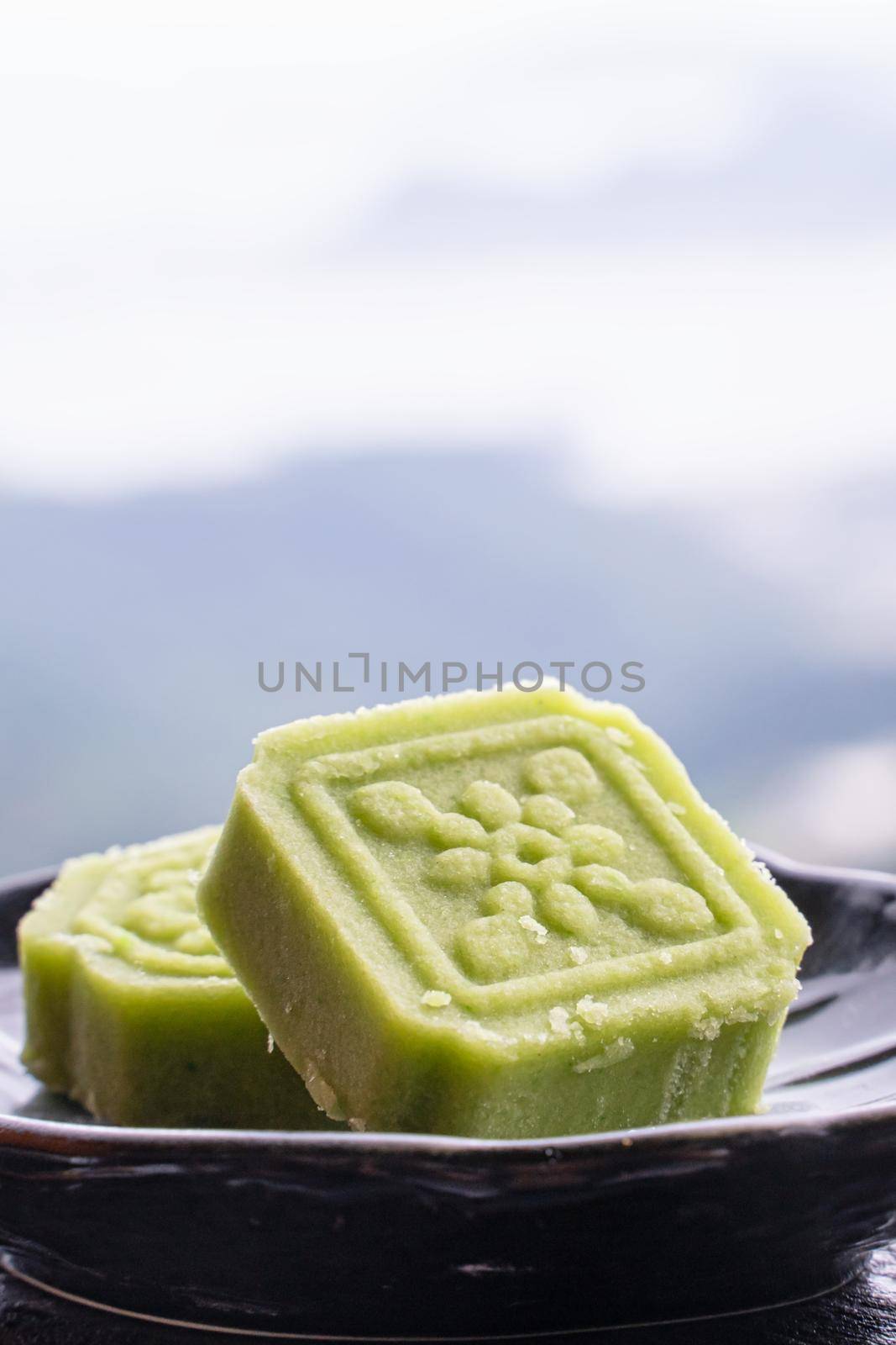 Delicious green mung bean cake with black tea plate on wooden railing of a teahouse in Taiwan with beautiful landscape in background, close up.