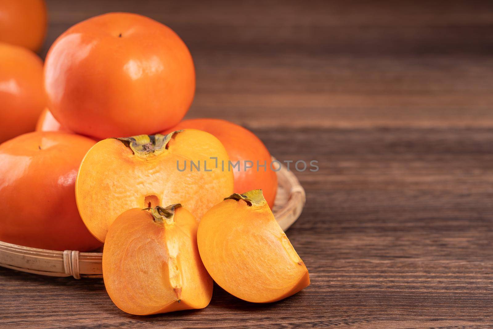Fresh, beautiful orange color persimmon kaki on bamboo sieve over dark wooden table. Seasonal, traditional fruit of Chinese lunar new year, close up.