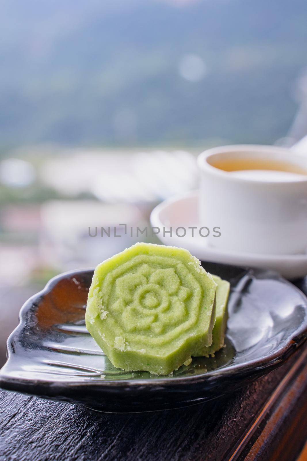 Delicious green mung bean cake with black tea plate on wooden railing of a teahouse in Taiwan with beautiful landscape in background, close up.