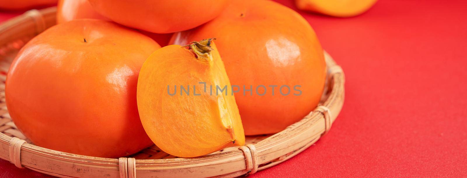 Fresh beautiful sliced sweet persimmon kaki isolated on red table background and bamboo sieve, Chinese lunar new year design concept, close up.