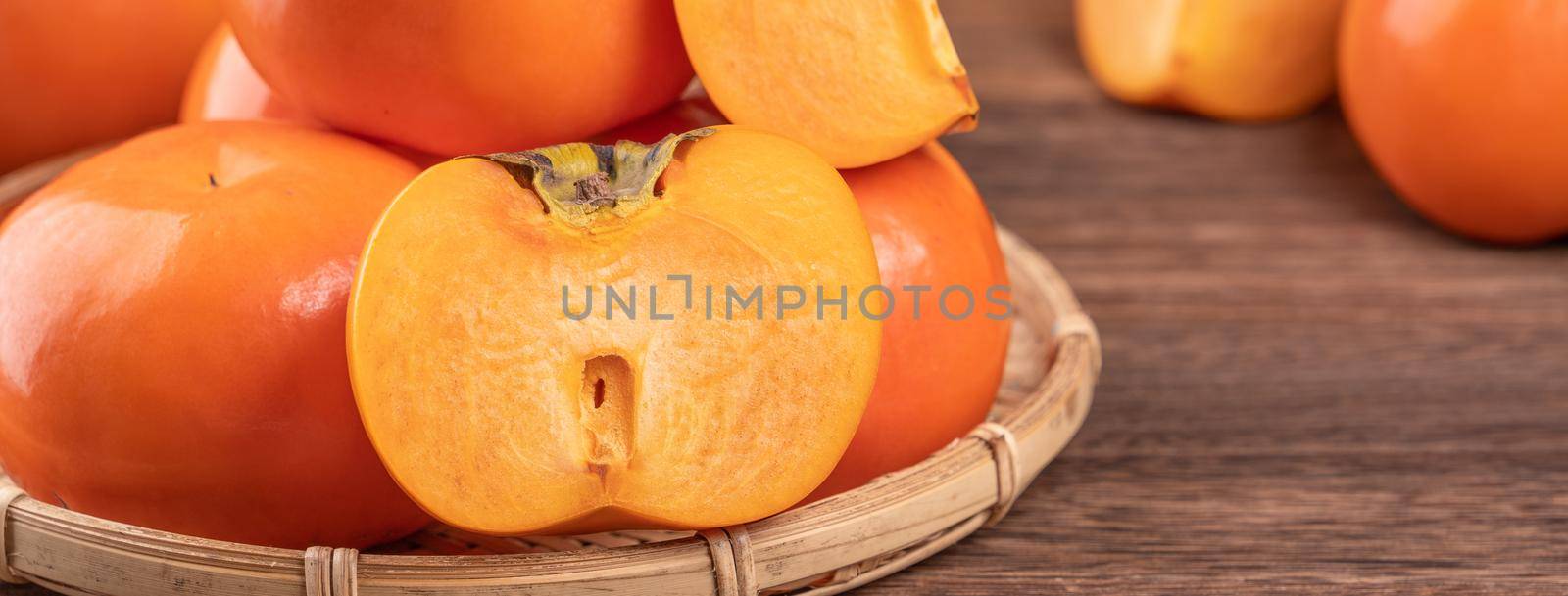 Fresh, beautiful orange color persimmon kaki on bamboo sieve over dark wooden table. Seasonal, traditional fruit of Chinese lunar new year, close up.