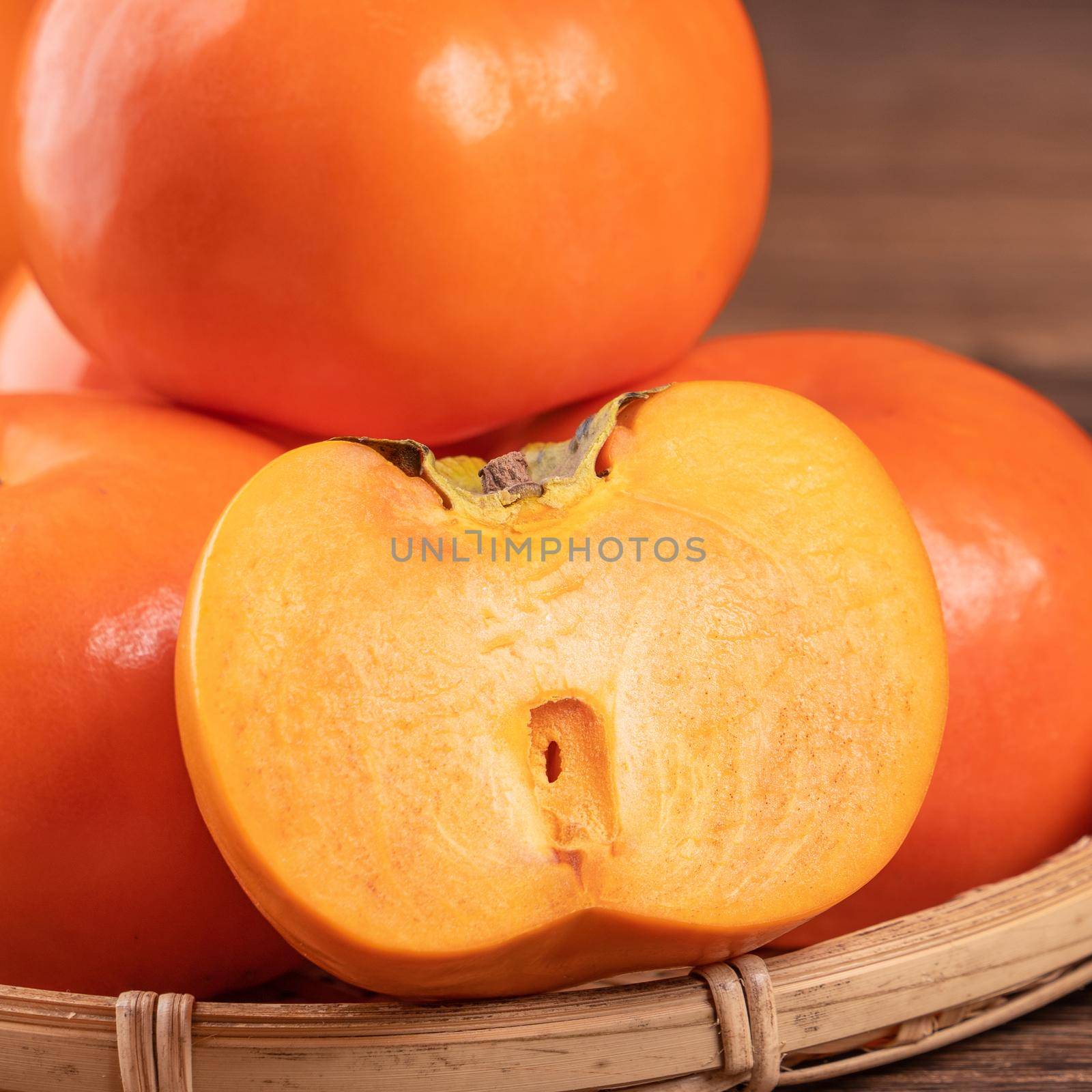 Fresh, beautiful orange color persimmon kaki on bamboo sieve over dark wooden table. Seasonal, traditional fruit of Chinese lunar new year, close up.