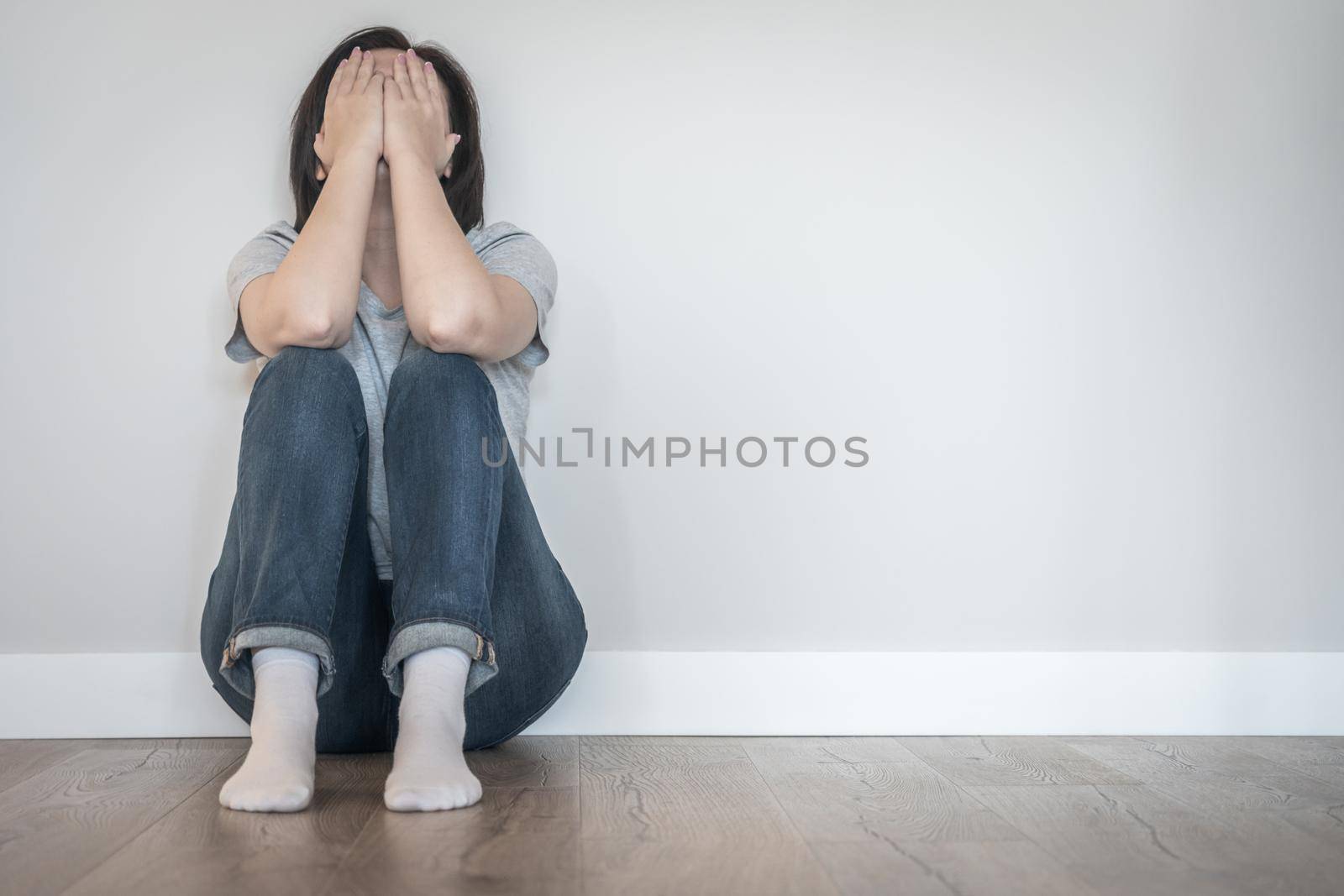 Sad woman sitting on a floor alone in empty room, despair and lonely