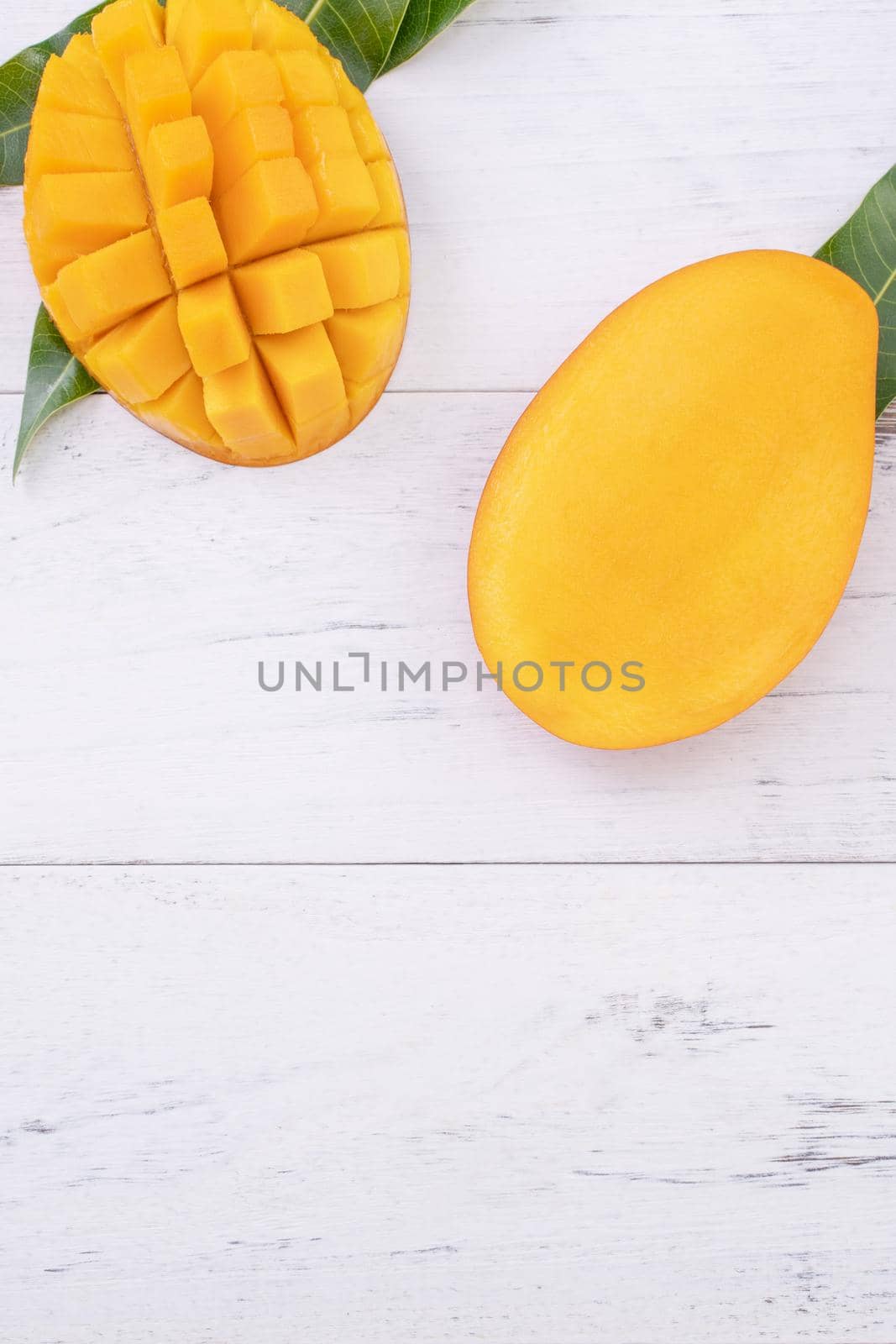 Beautiful chopped ripe mango with green leaves on bright white color wooden background, top view, flat lay, copy space. Tropical fruit design concept.