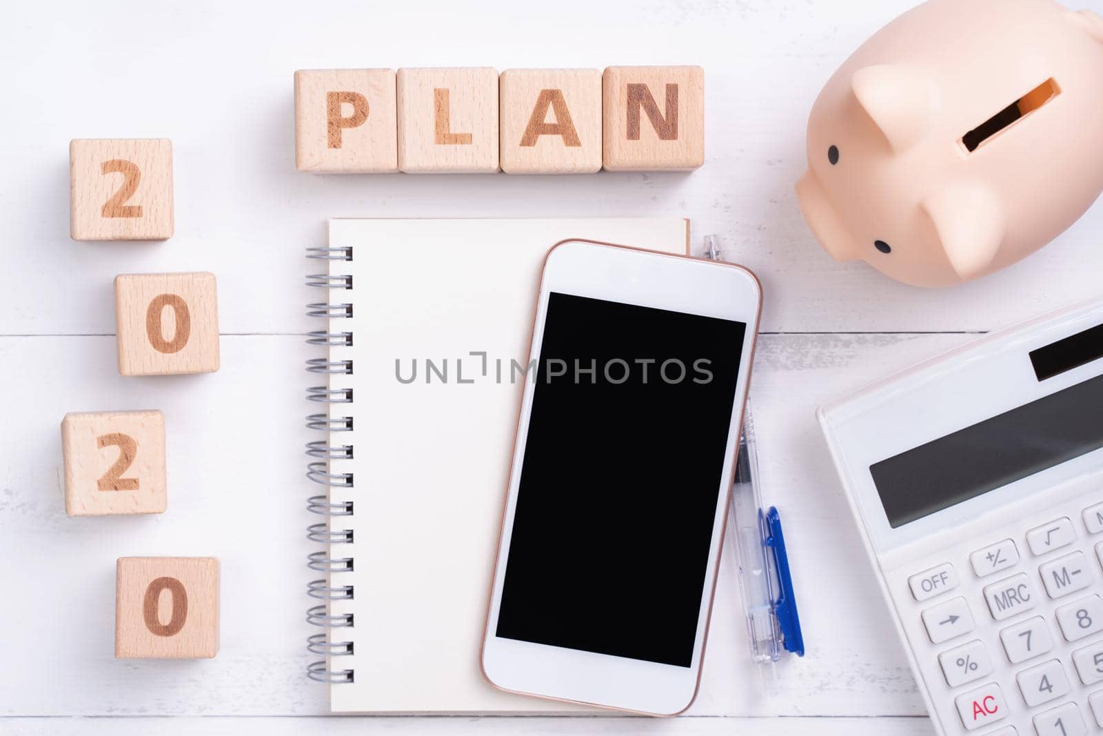 2020 goal, finance plan abstract design concept, wood blocks on white table background with piggy bank, cell phone, top view, flat lay, copy space.