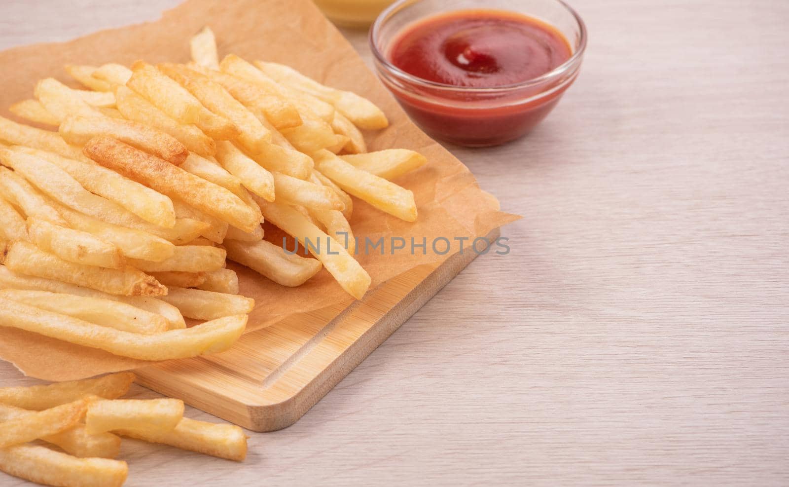 Golden yummy deep French fries on kraft baking sheet paper and serving tray to eat with ketchup and yellow mustard, top view, lifestyle.
