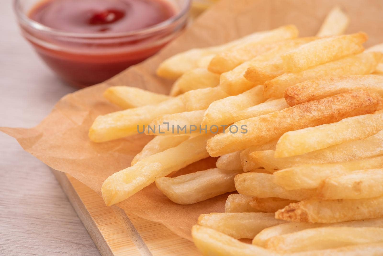 Golden yummy deep French fries on kraft baking sheet paper and serving tray to eat with ketchup and yellow mustard, top view, lifestyle.