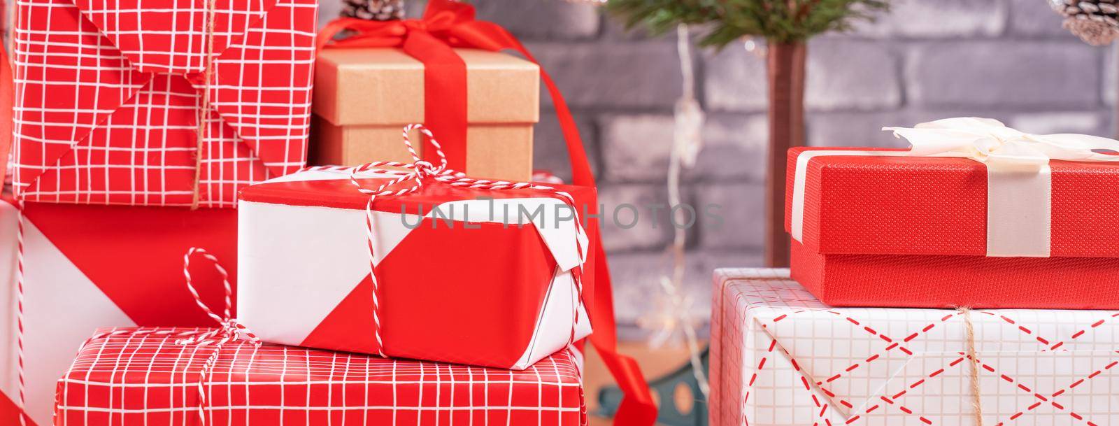 Decorated Christmas tree with wrapped beautiful red and white gifts at home with black brick wall, festive design concept, close up.