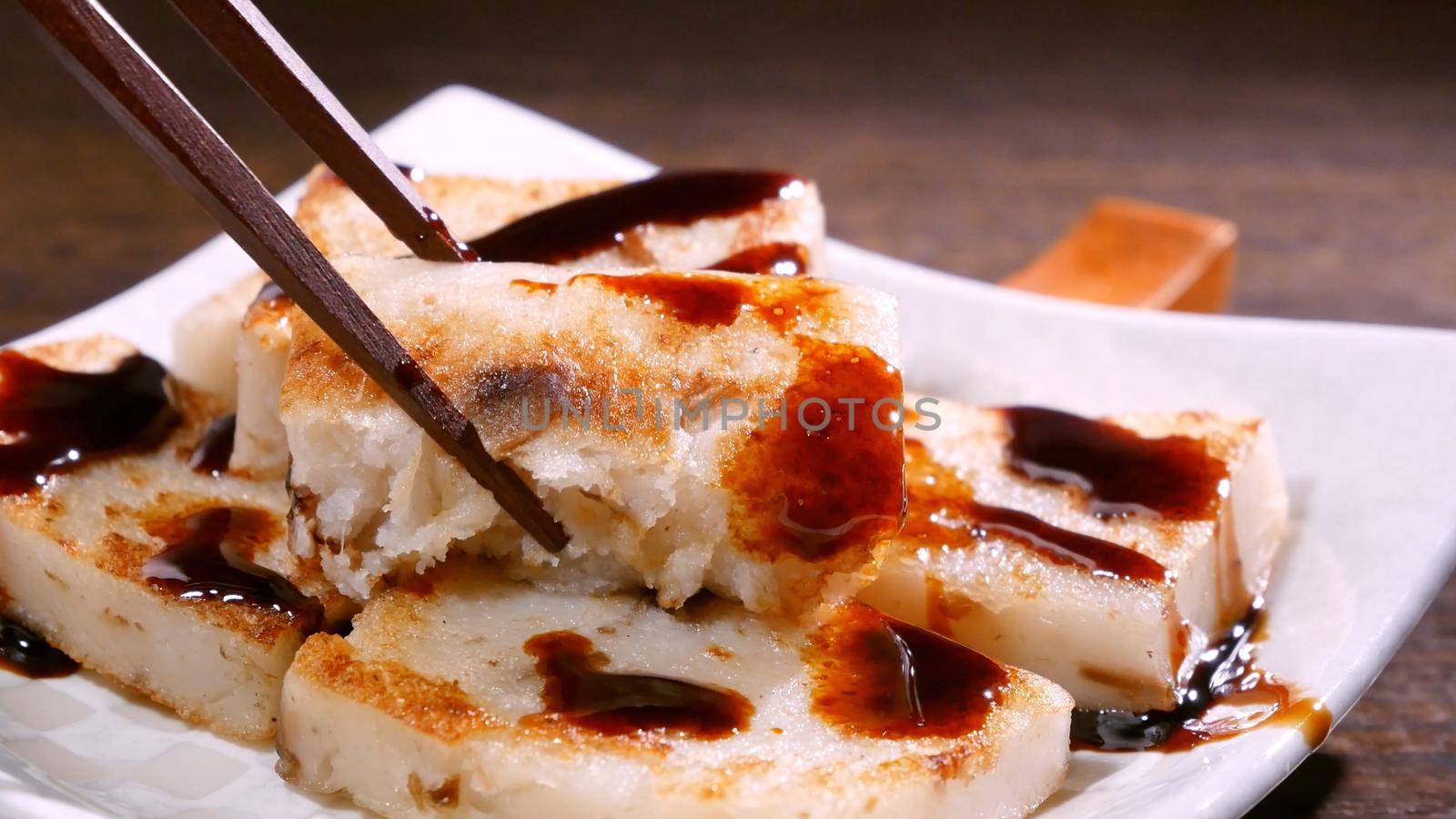 Pouring black soy sauce on ready-to-eat delicious turnip cake, Chinese traditional local dish radish cake in restaurant, close up, copy space.