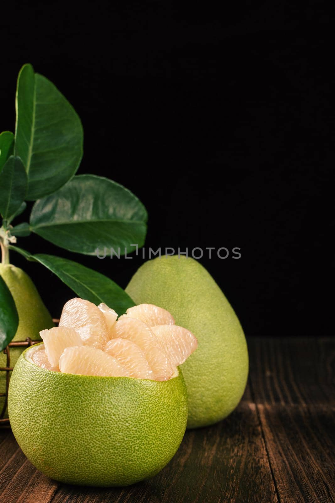 Fresh peeled pomelo, grapefruit, shaddock with green leaves on dark wooden plank table. Seasonal fruit near mid-autumn festival, close up, copy space by ROMIXIMAGE