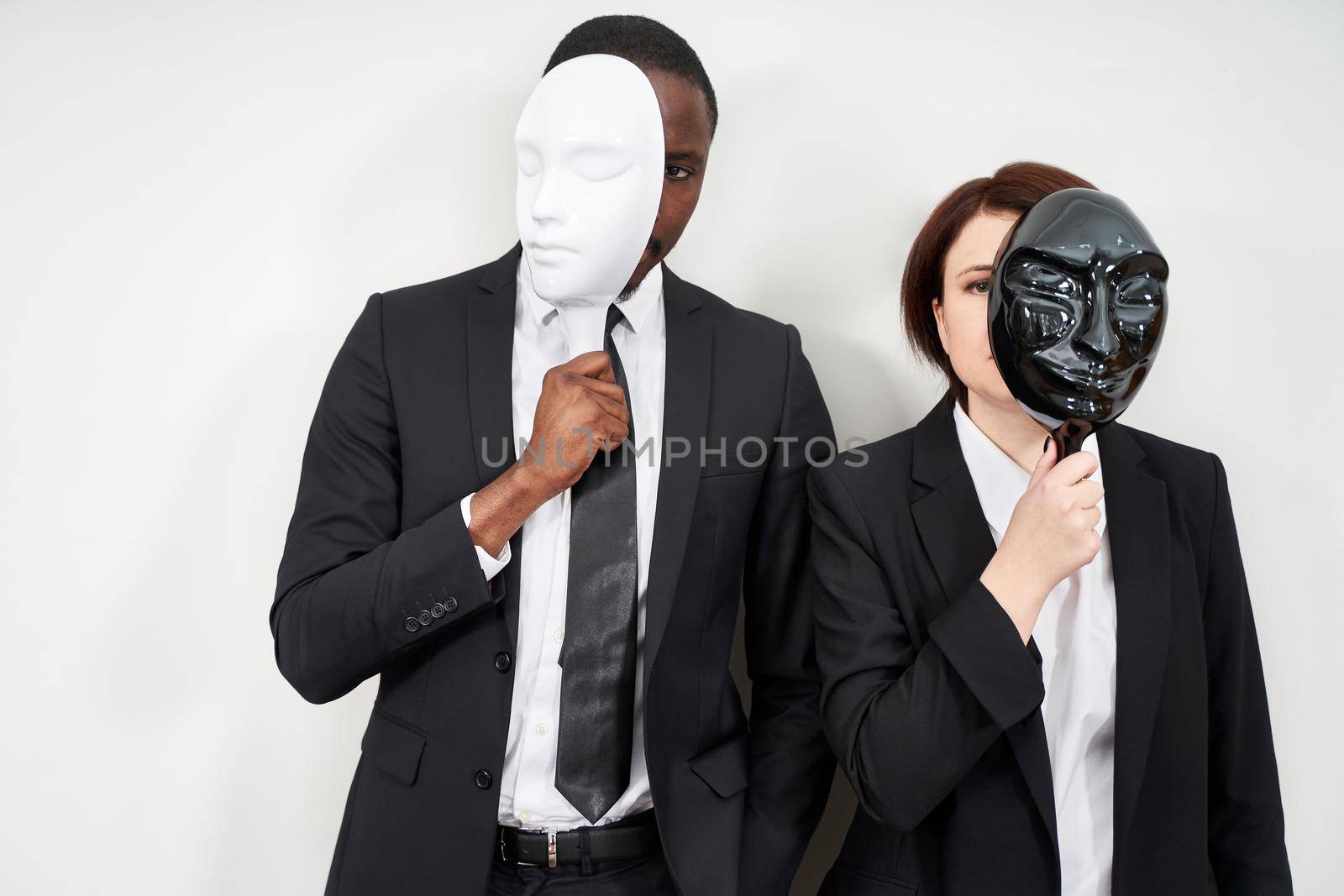 African man and Caucasian woman wearing black suits hiding face with masks