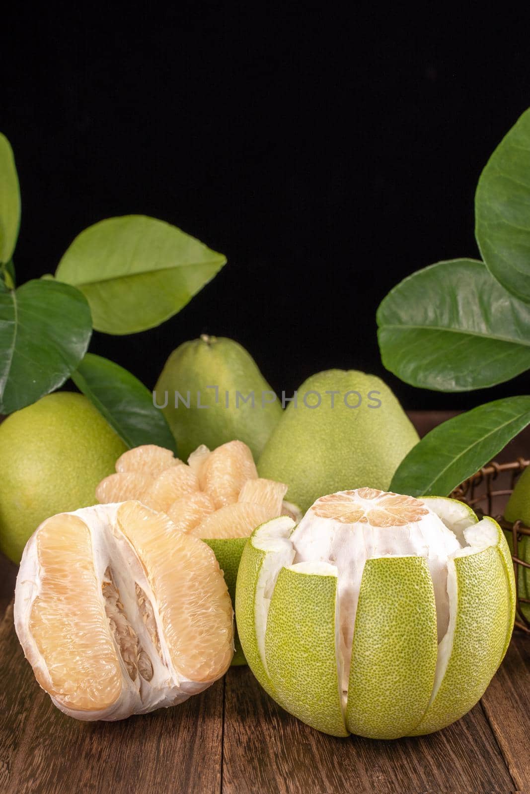 Fresh peeled pomelo, grapefruit, shaddock with green leaves on dark wooden plank table. Seasonal fruit near mid-autumn festival, close up, copy space