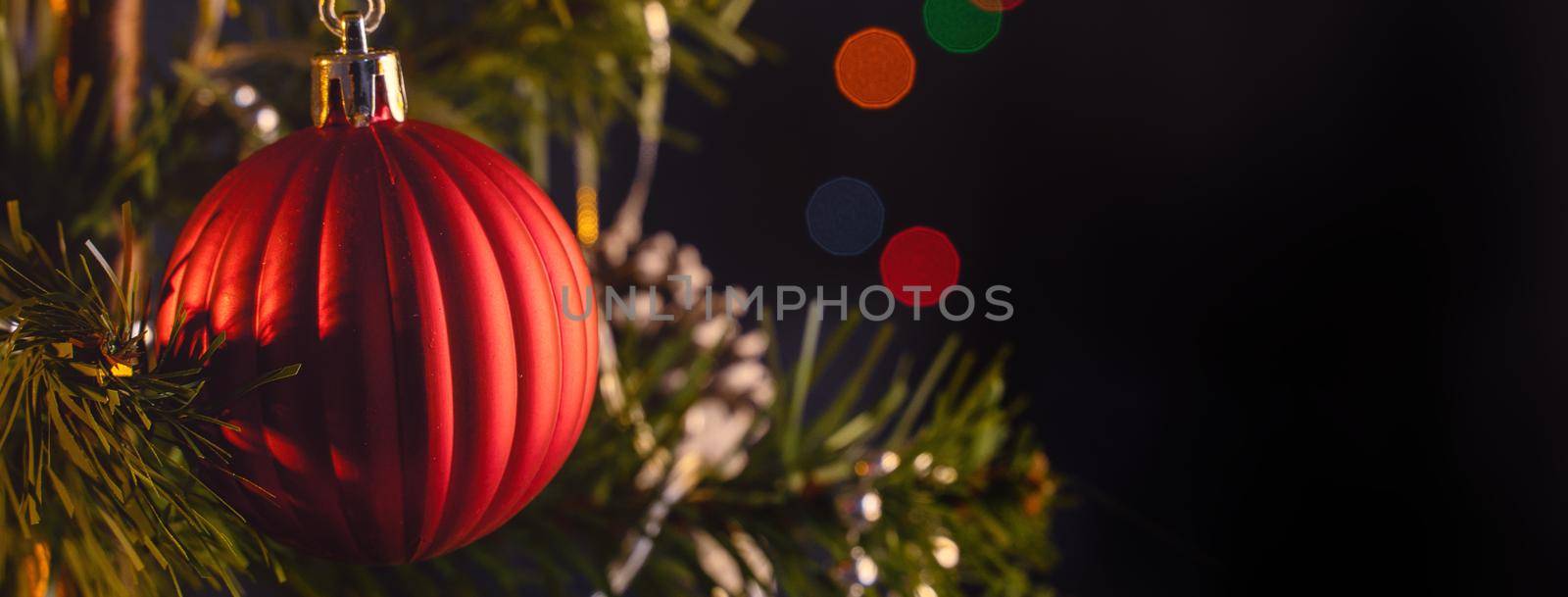 Beautiful Christmas decor concept, bauble hanging on the Christmas tree with sparkling light spot, blurry dark black background, macro detail, close up.