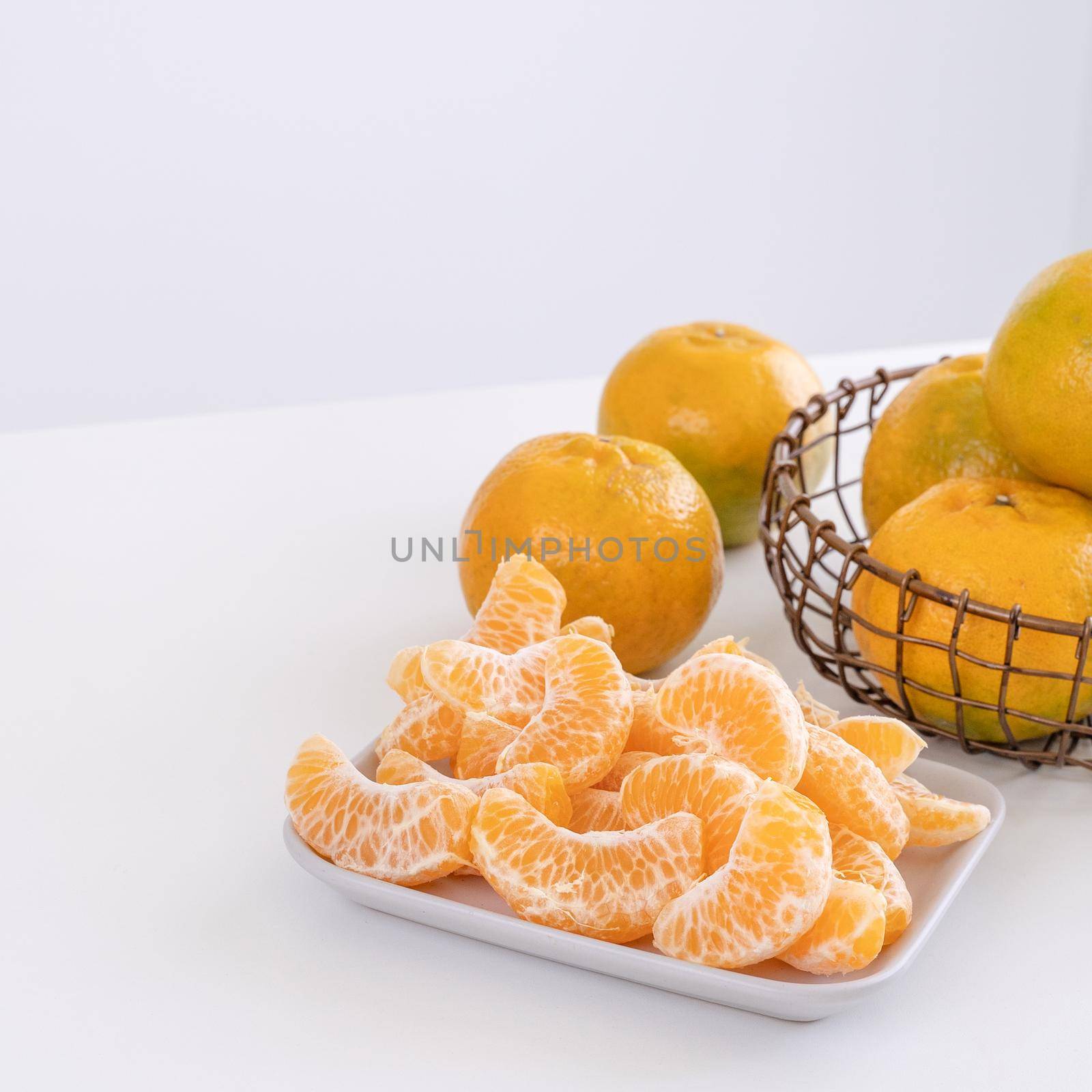 Beautiful peeled tangerines in a plate and metal basket isolated on bright white clean table in a modern contemporary kitchen island, close up.