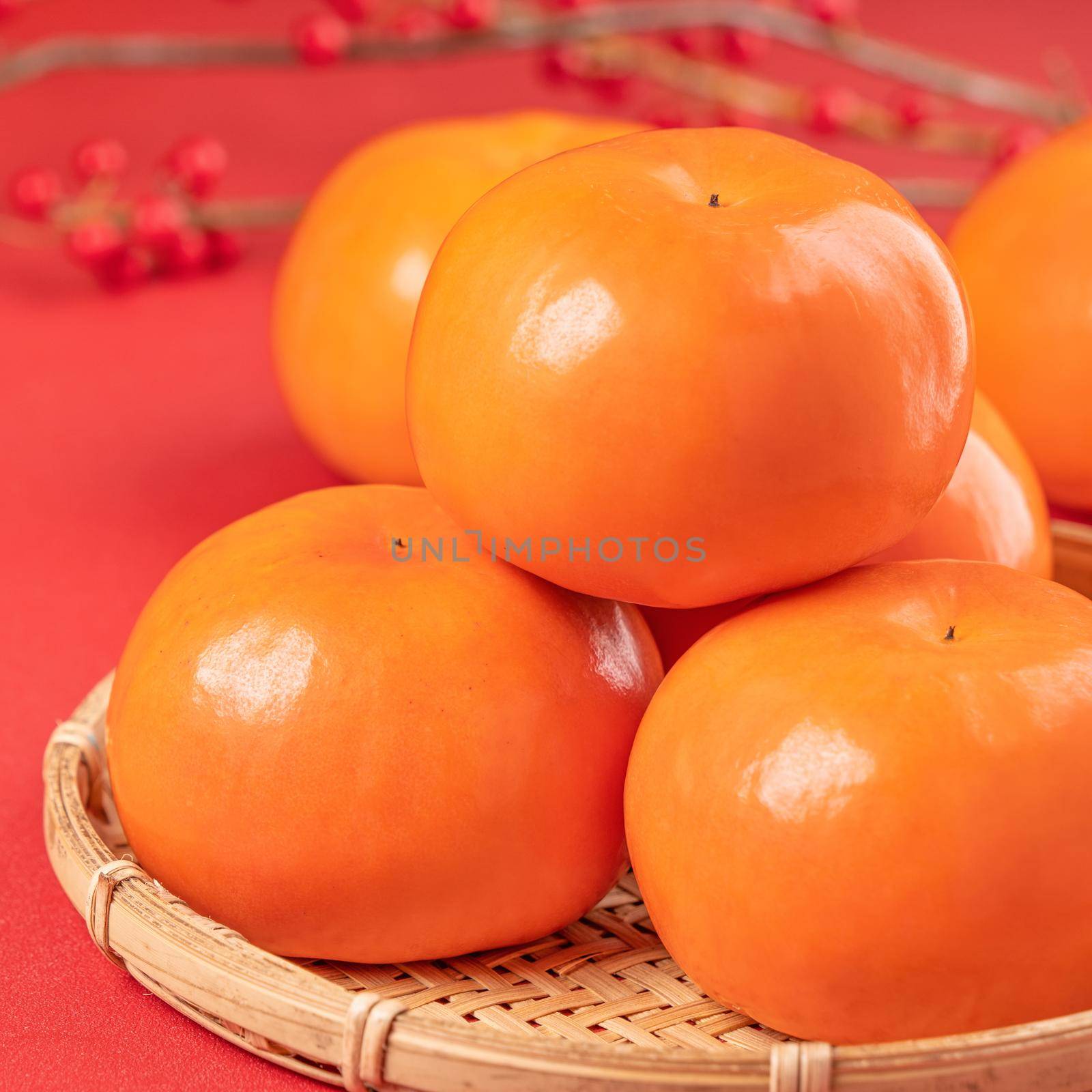 Fresh beautiful sliced sweet persimmon kaki isolated on red table background and bamboo sieve, Chinese lunar new year design concept, close up. by ROMIXIMAGE