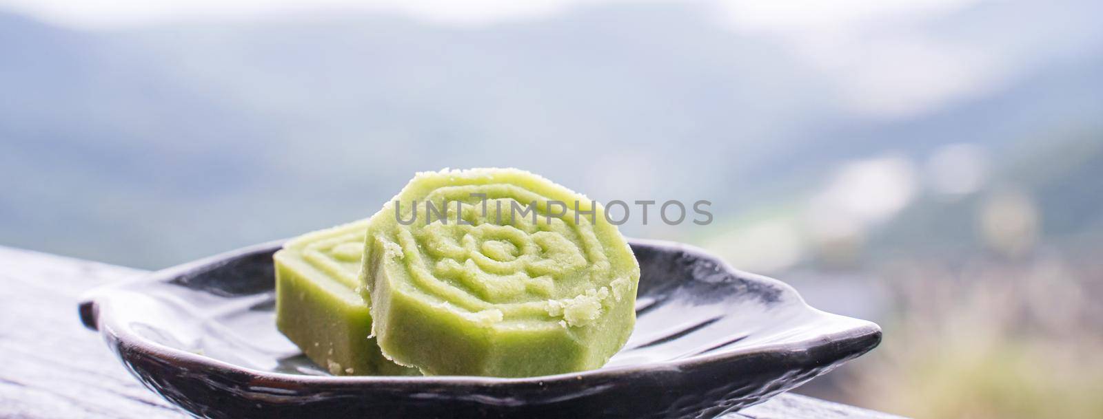Delicious green mung bean cake with black tea plate on wooden railing of a teahouse in Taiwan with beautiful landscape in background, close up. by ROMIXIMAGE