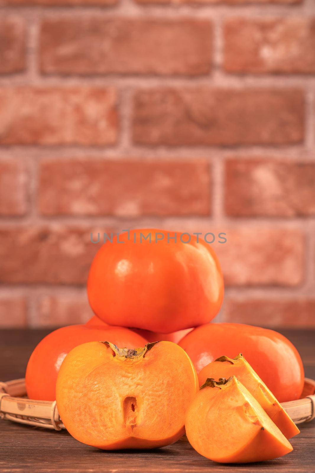 Fresh beautiful sliced sweet persimmon kaki on dark wooden table with red brick wall background, Chinese lunar new year fruit design concept, close up. by ROMIXIMAGE