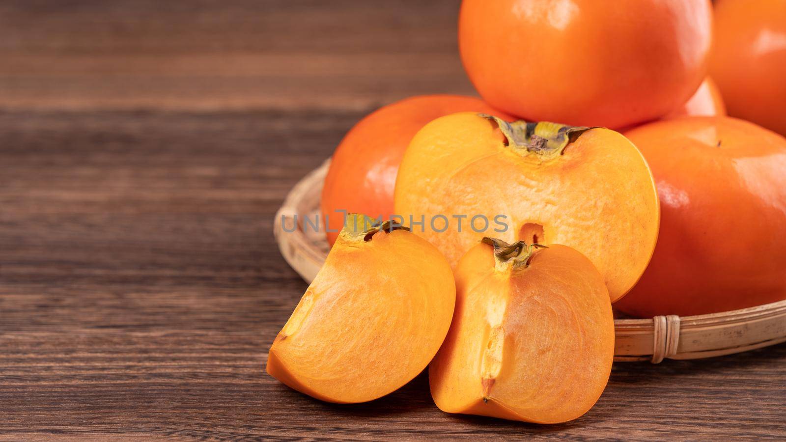 Fresh, beautiful orange color persimmon kaki on bamboo sieve over dark wooden table. Seasonal, traditional fruit of Chinese lunar new year, close up.