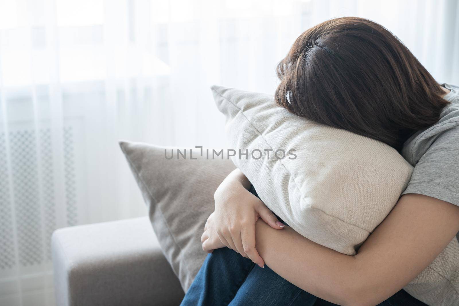 Sad depressed woman at home, she is sitting on the couch and hugging a pillow, loneliness and sadness concept