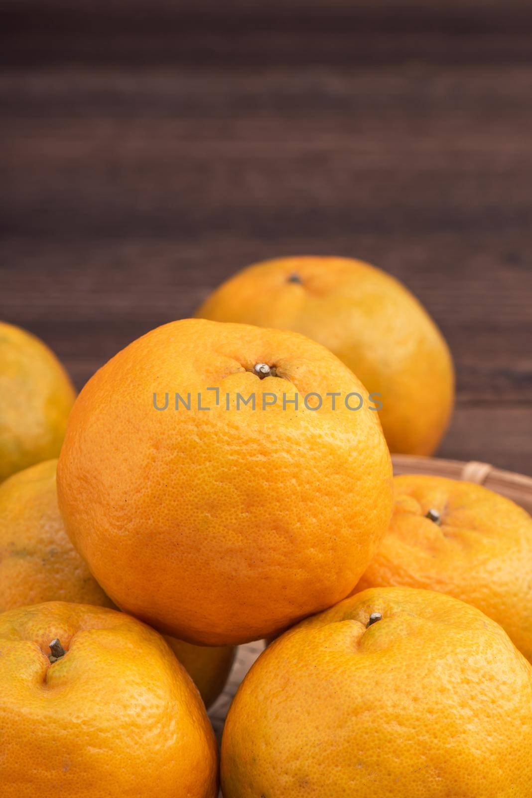 Fresh, beautiful orange color tangerine on bamboo sieve over dark wooden table. Seasonal, traditional fruit of Chinese lunar new year, close up.