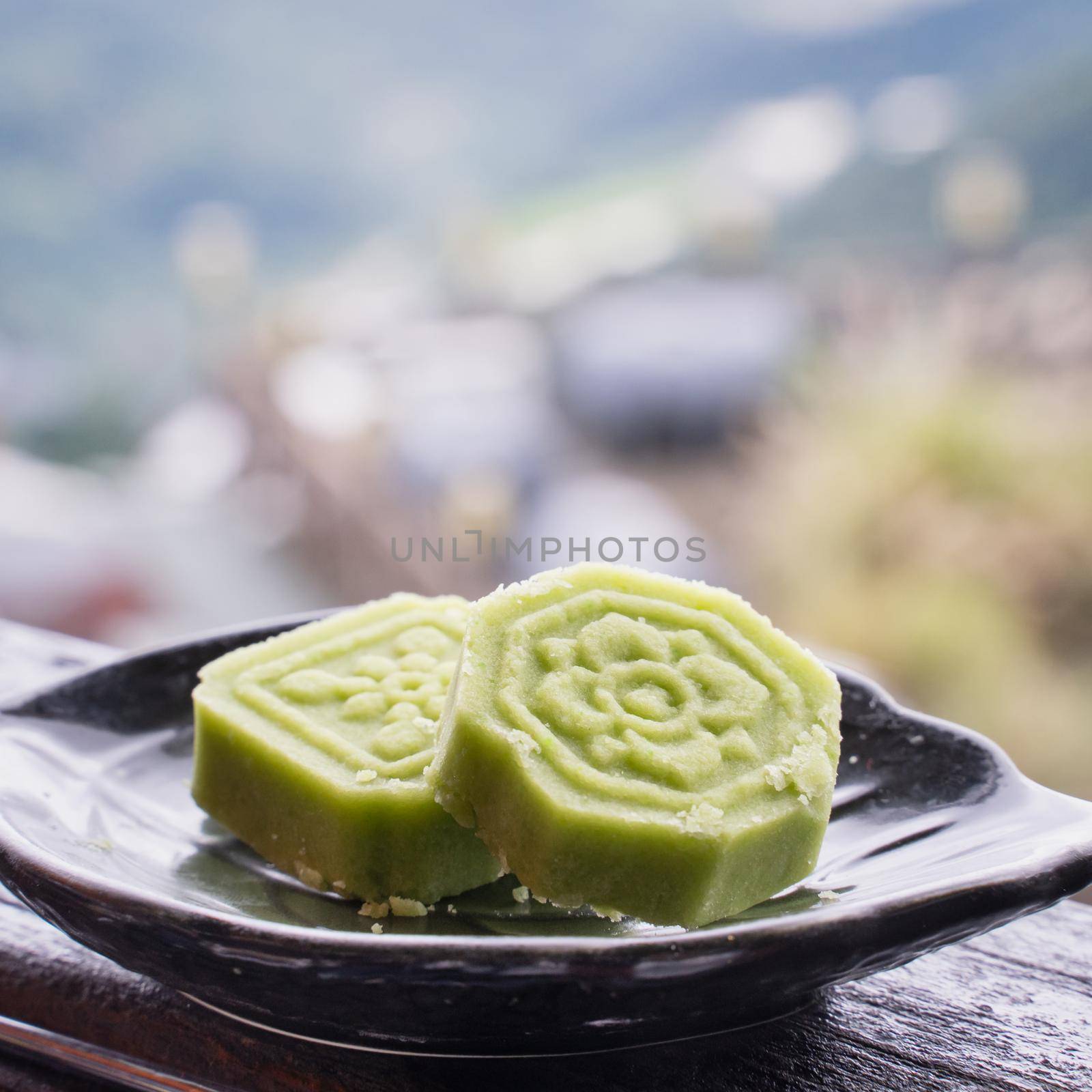 Delicious green mung bean cake with black tea plate on wooden railing of a teahouse in Taiwan with beautiful landscape in background, close up.