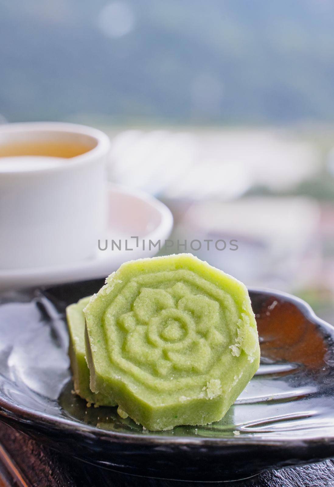 Delicious green mung bean cake with black tea plate on wooden railing of a teahouse in Taiwan with beautiful landscape in background, close up.