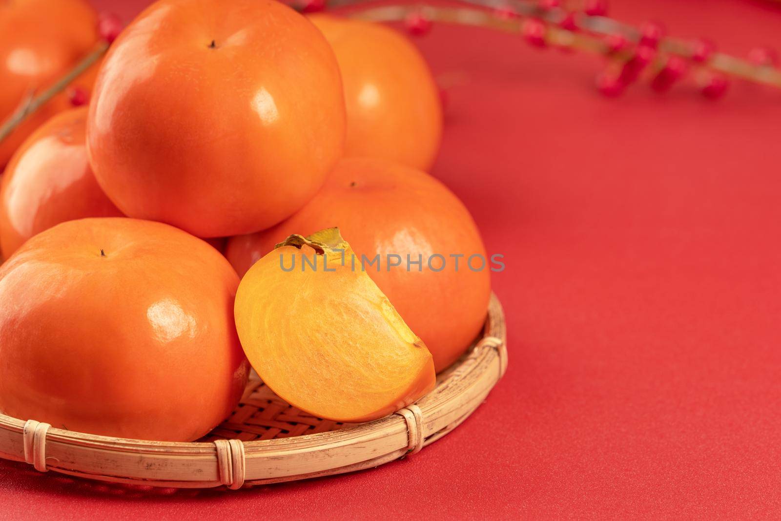 Fresh beautiful sliced sweet persimmon kaki isolated on red table background and bamboo sieve, Chinese lunar new year design concept, close up.