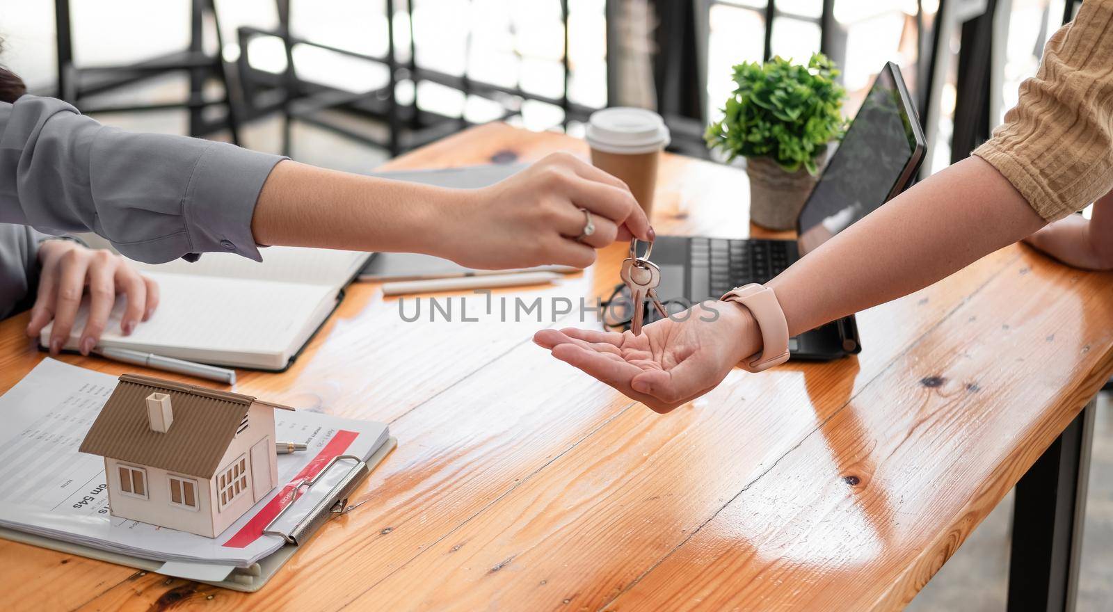 real estate agent holding house key to his client after signing contract agreement in office,concept for real estate, moving home or renting property.