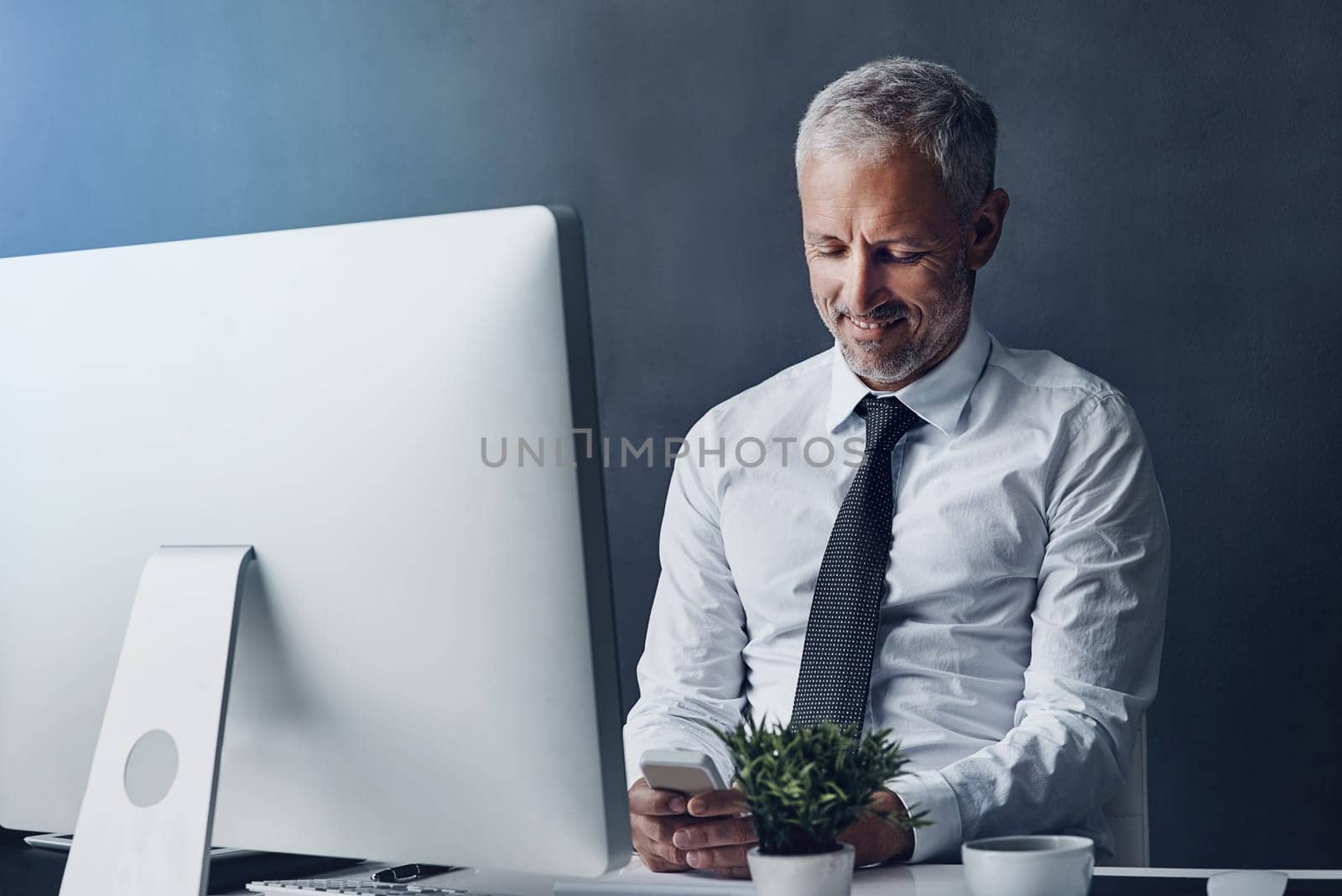 Replying to a text. a mature businessman sending a text while working on his computer. by YuriArcurs