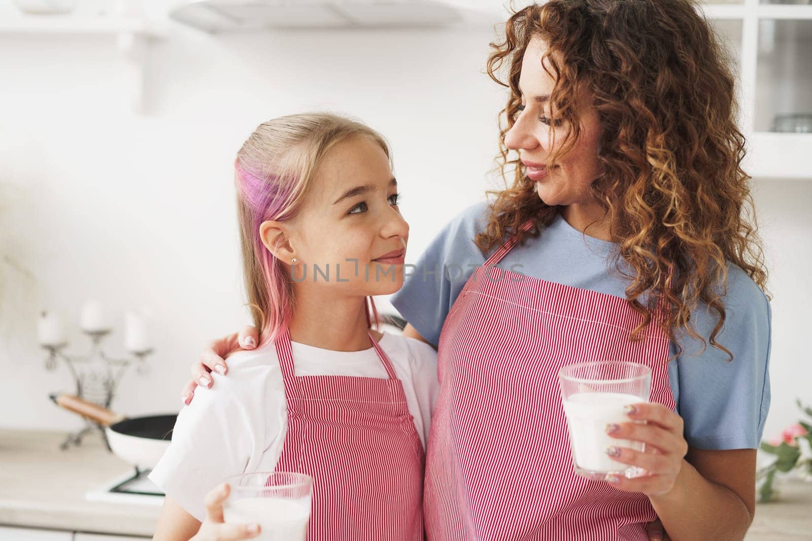 Mother and daughter smiling and holding glasses of milk in kitchen, close up