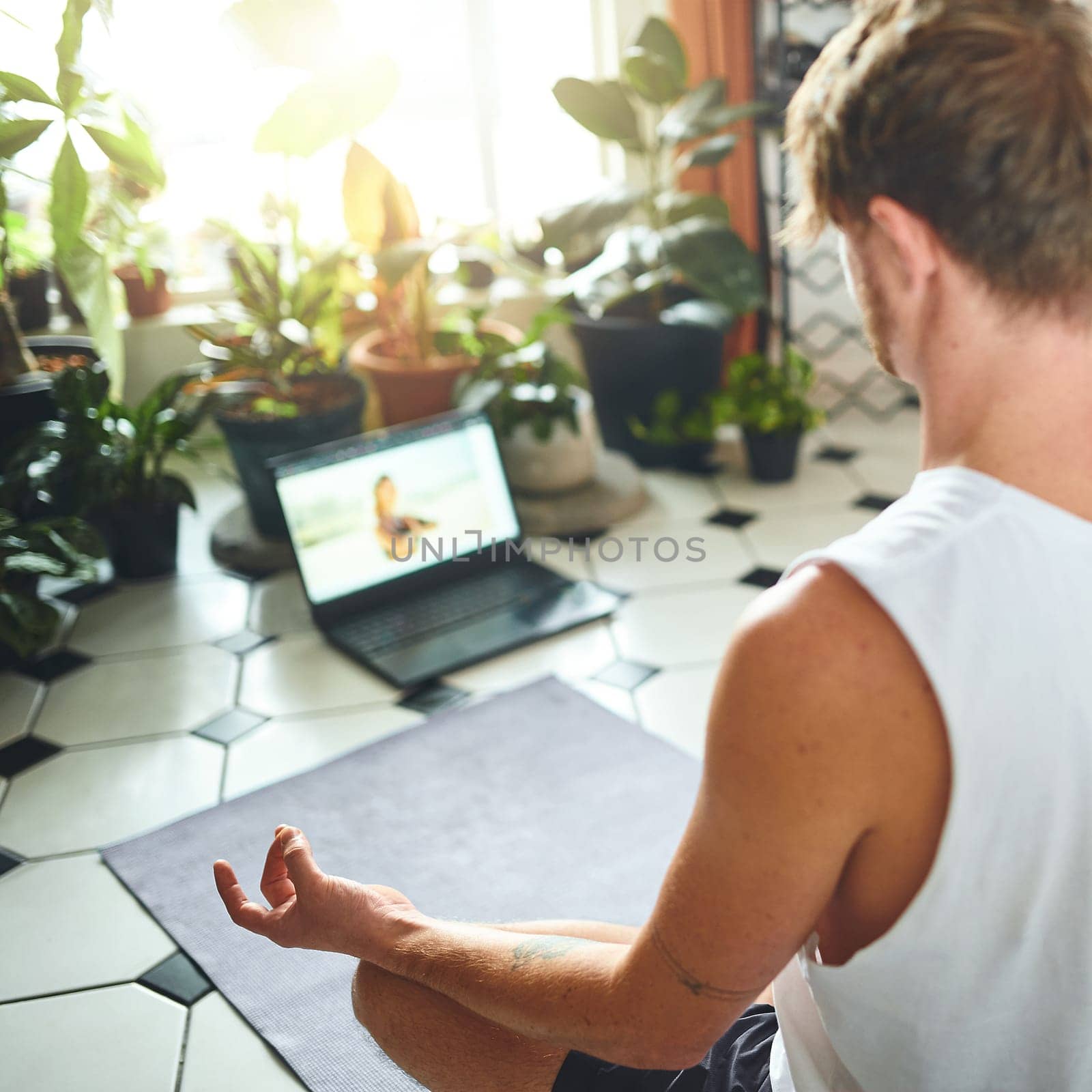 Yoga class brought straight to you. a young man using a laptop while meditating in the lotus position at home. by YuriArcurs