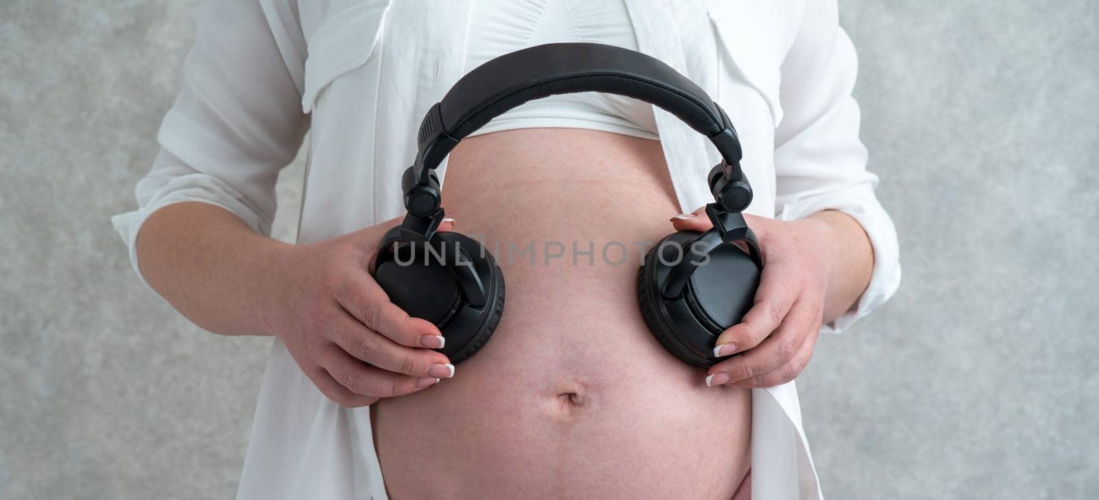 Panorama of Pregnant woman playing music to her baby through headphones putting them on her belly by Mariakray