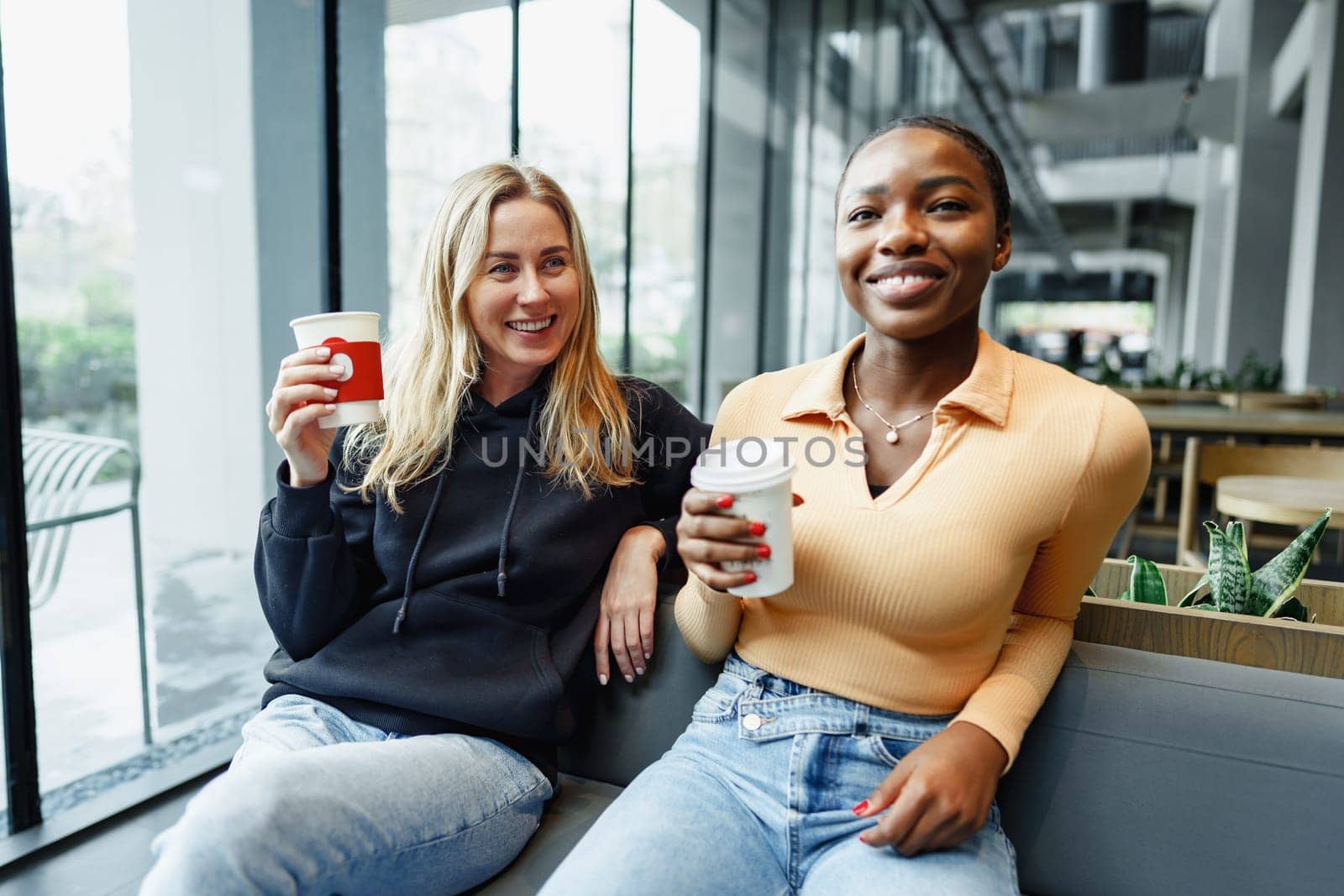 Two young women friends enjoying coffee together in a coffee shop by Fabrikasimf