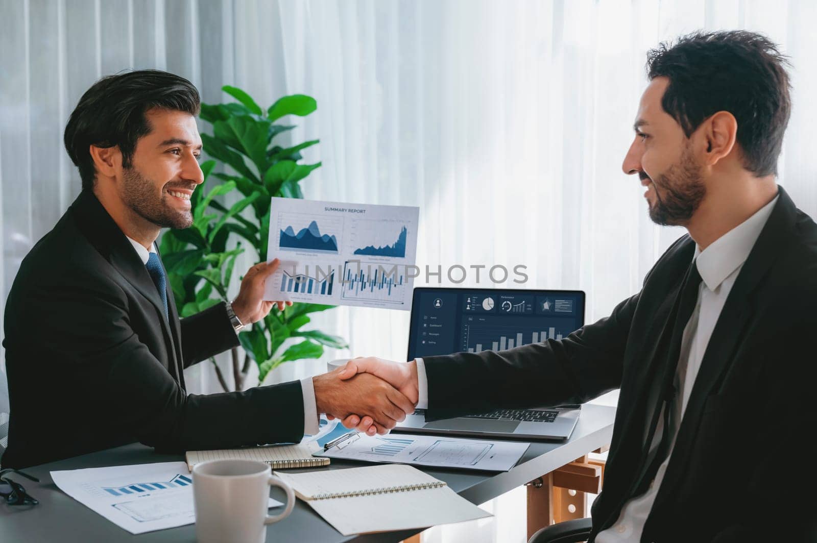 Closeup professional businessman shaking hands over desk in modern office after successfully analyzing pile of dashboard data paper as teamwork and integrity handshake in workplace concept. fervent