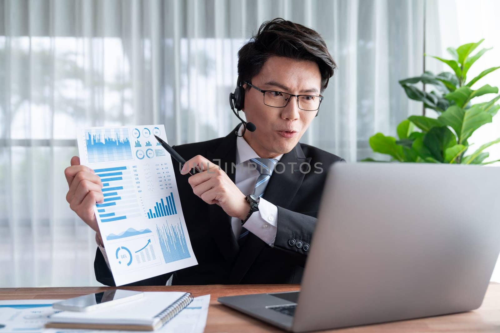Confident asian telesales businessman work in modern office wearing headphone, presenting BI dashboard analysis to clients and customers in online meeting. Success modern telesales business . Jubilant