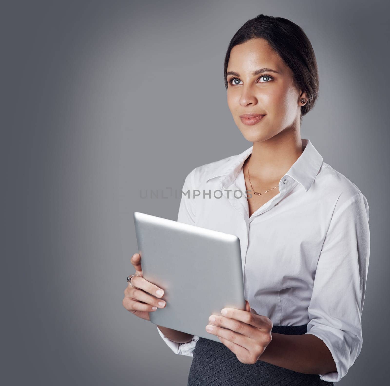 Staying organized and connected with cutting edge technology. Studio shot of a young businesswoman using a digital tablet against a gray background. by YuriArcurs