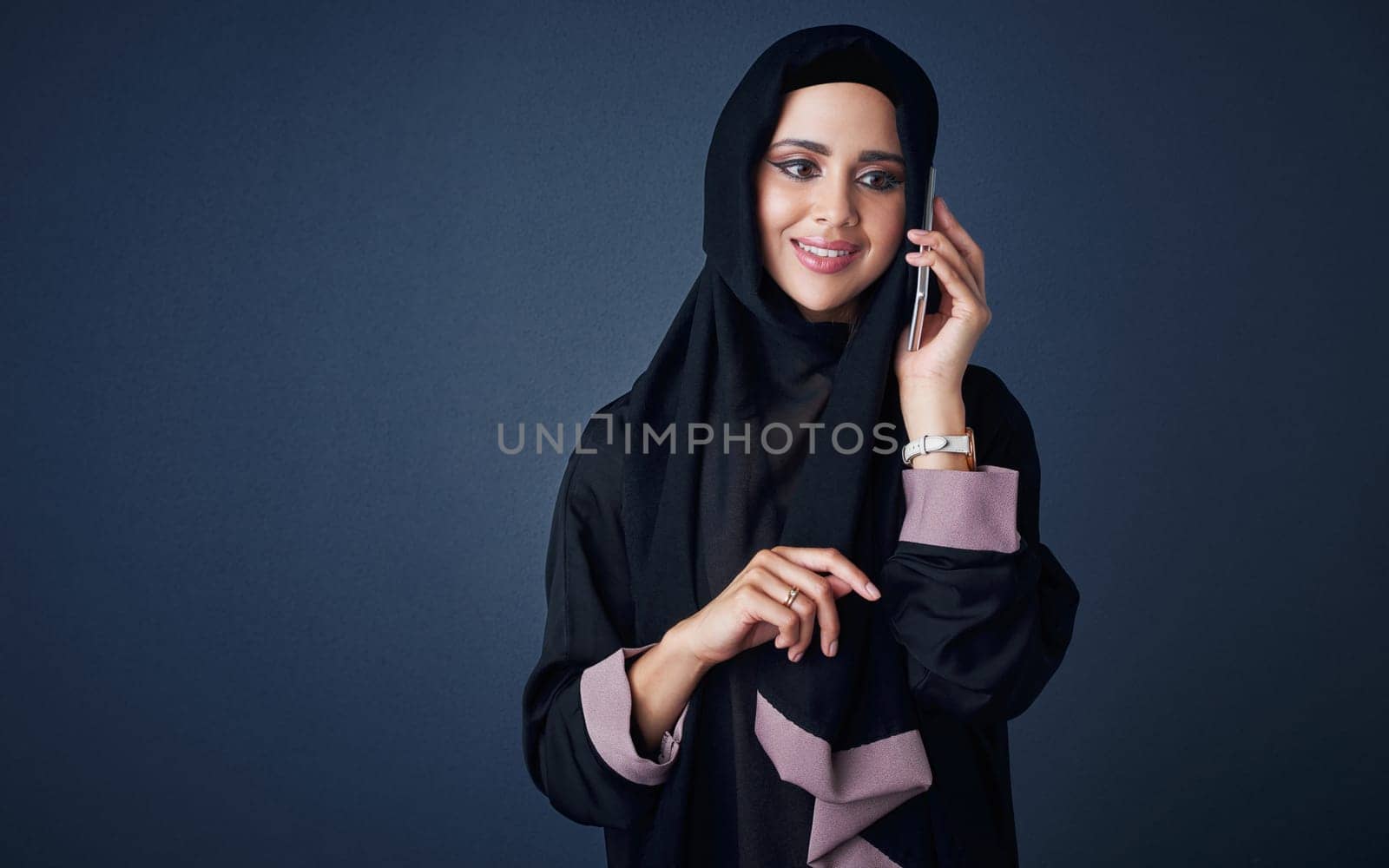 Stay in contact, stay happy. Studio shot of a young woman wearing a burqa and using a mobile phone against a gray background. by YuriArcurs