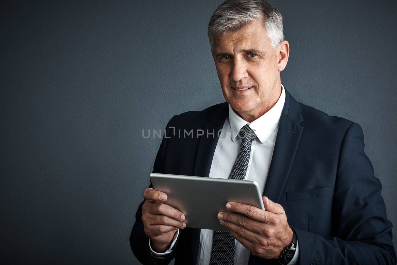 I use it for business and pleasure. Studio shot of a mature businessman using his digital tablet. by YuriArcurs